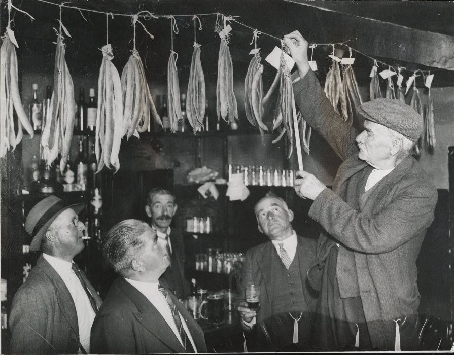 Man holding up runner beans to a crowd in a pub