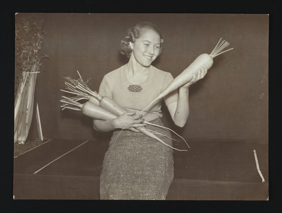 Woman holding three oversized carrots