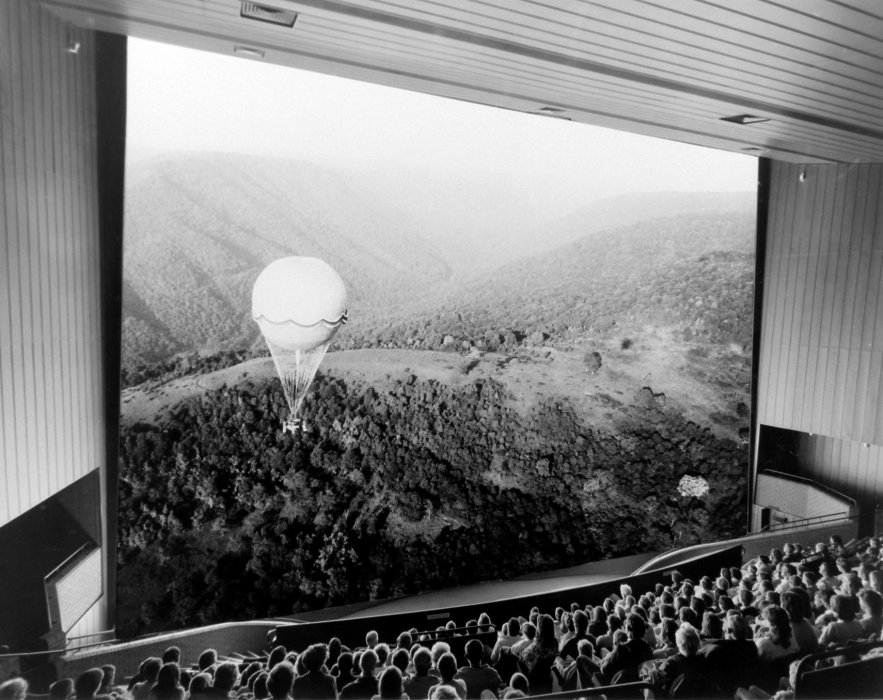 A black and white photograph of an audience looking at an IMAX cinema screen