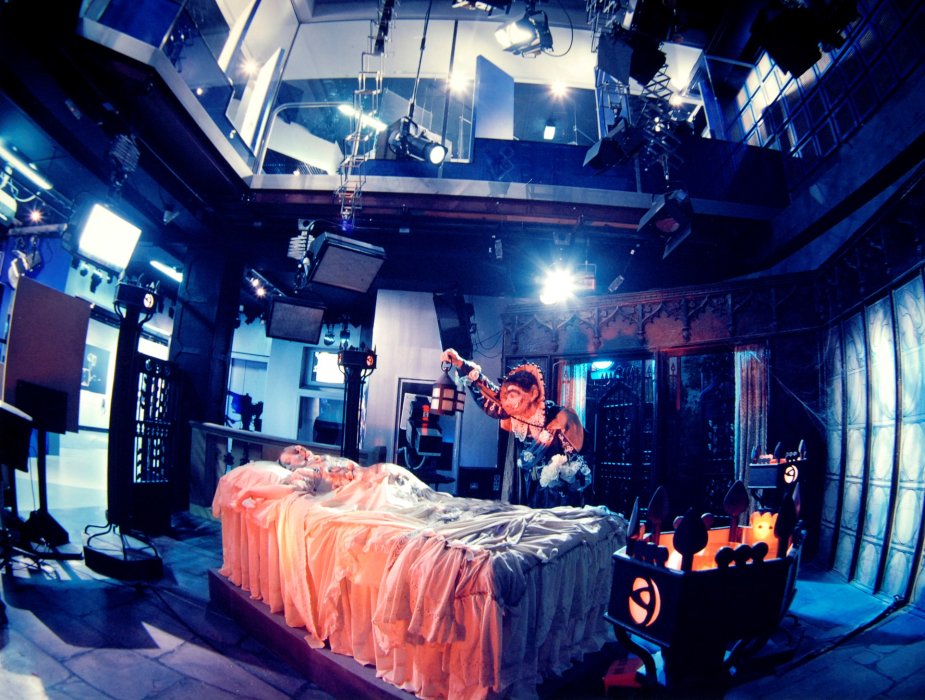 A woman lies on a bed on a sound stage with a man dressed as Dracula leaning over her
