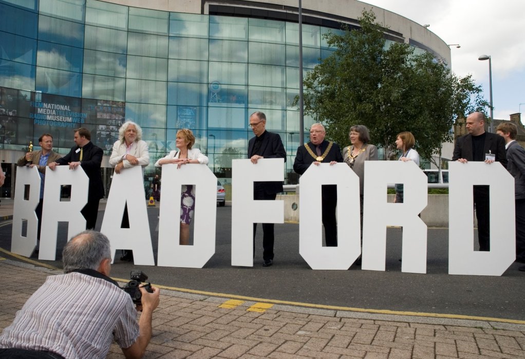 A group of people standing behind large letters spelling Bradford, in front of the Museum