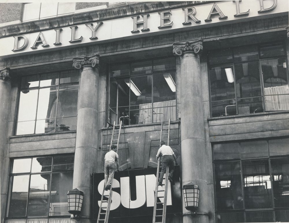 Workers adding a sign for the Sun to the main Daily Herald editorial building on Endell Street, London
