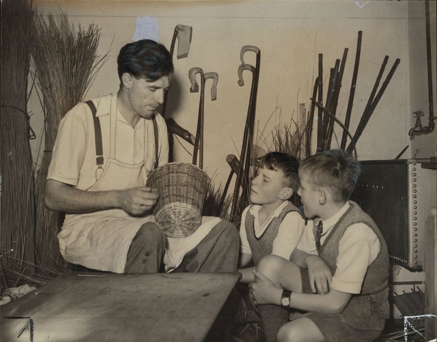 Man making a basket, watched by two children