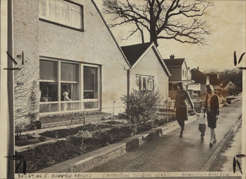 Couple with a child walking past a house with a poodle sitting in the window