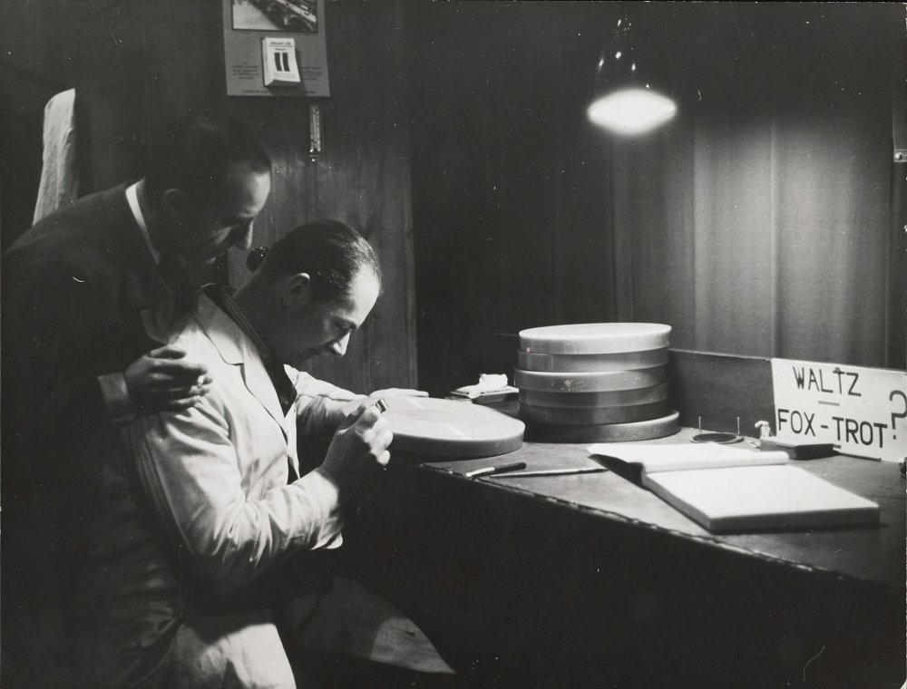 Two men study the grooves cut in a wax disc