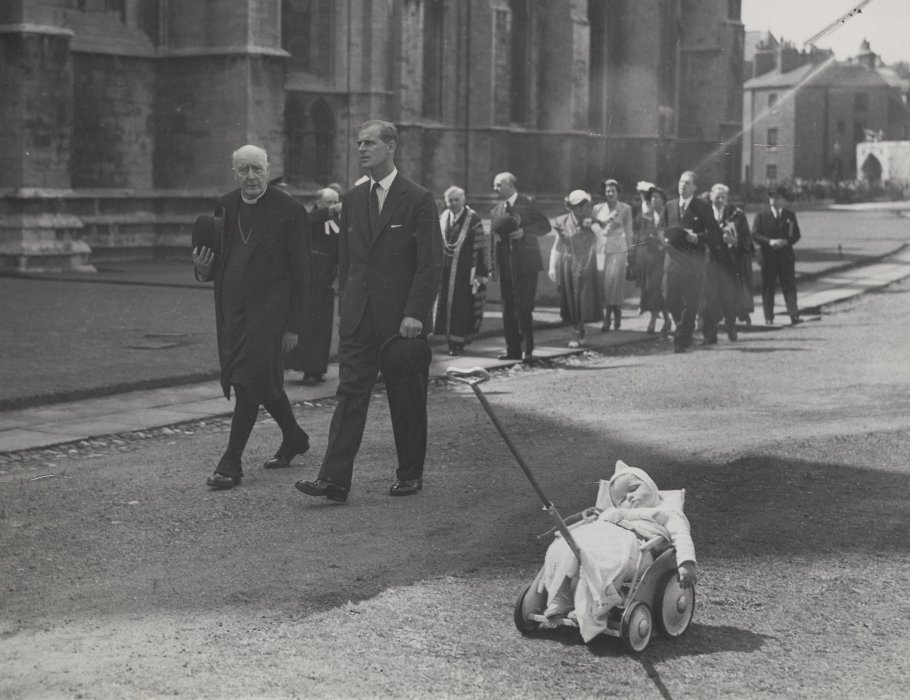 Baby asleep in pushchair in foreground, with Duke of Edinburgh and Archbishop of York pictured in the background