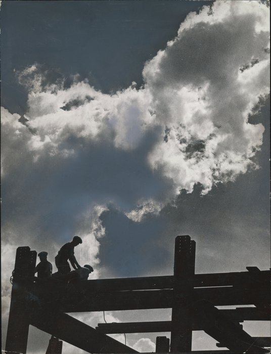 Silhouette of steel worker sitting on scaffolding against cloudy sky