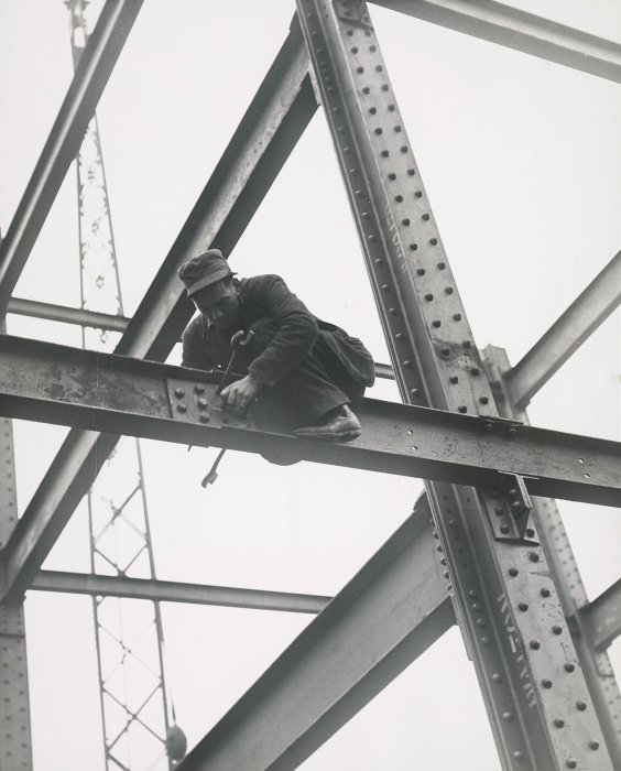 Worker bolts together steel girders on high scaffolding