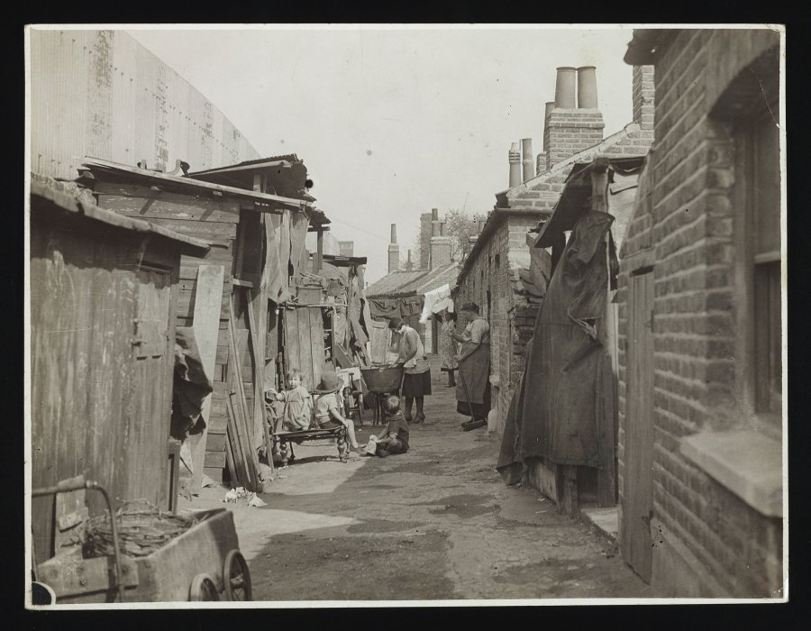 Women doing chores and children playing on a street of derelict housing