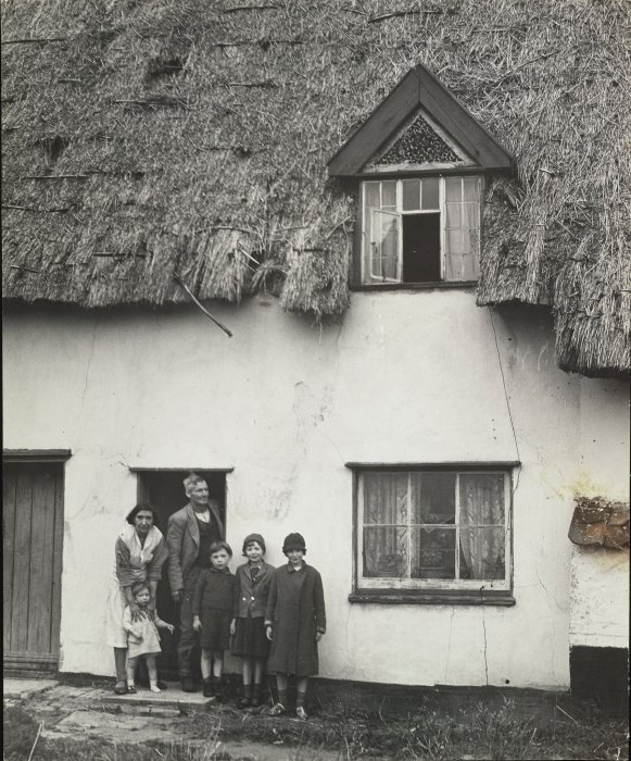 Man, woman and four children standing outside thatched cottage