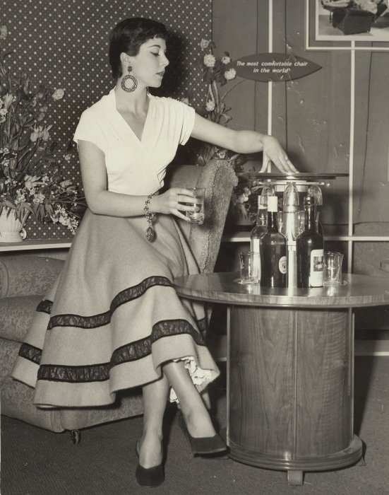 Alison White, American stage star, posing next to a cocktail cabinet at the Ideal Home Exhibition, 1954
