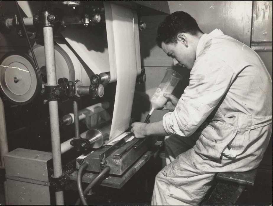 Factory worker applying emulsion to photographic paper from a bottle