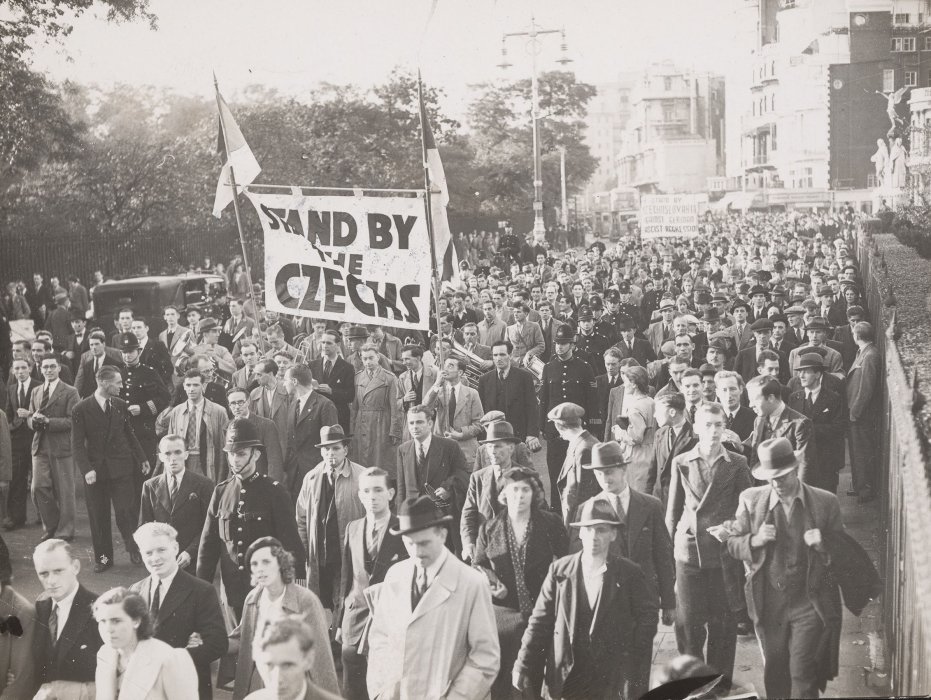 Crowd of protestors, flanked by police officers; some protestors carry a banner reading 'Stand By the Czechs'