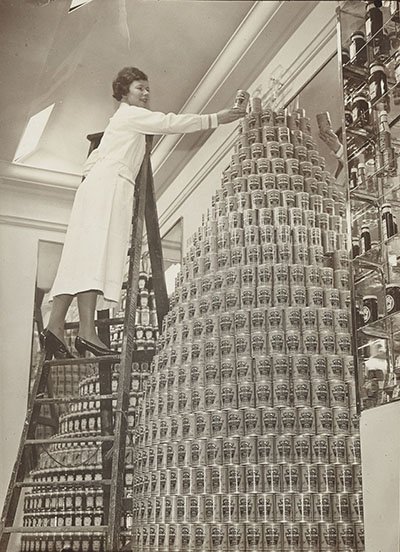 Woman placing cans of Heinz soup on top of a large stack