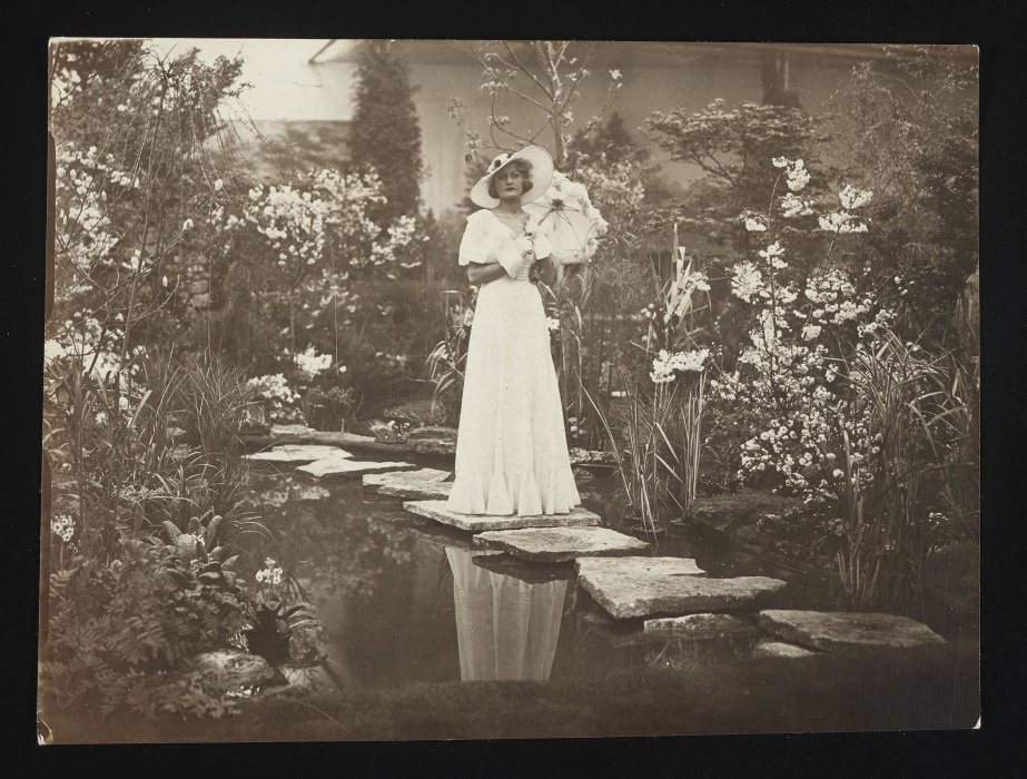 Model in white dress, holding parasol, in water garden