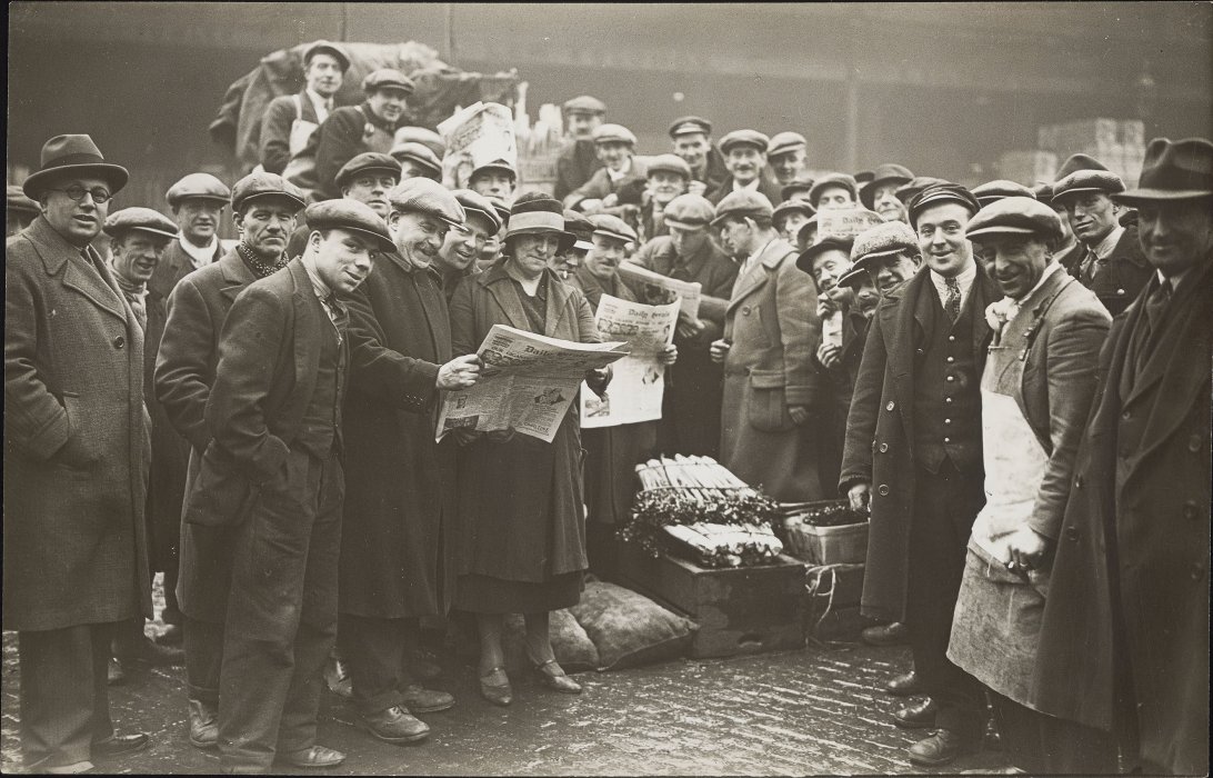 A large crowd of Covent Garden porters, men wearing hats and coats, facing the camera, some holding copies of the Daily Herald newspaper