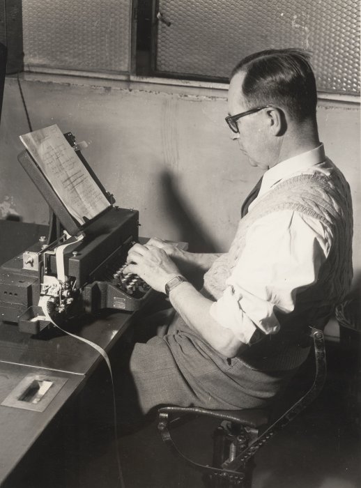 A man typing on a teleprinter machine